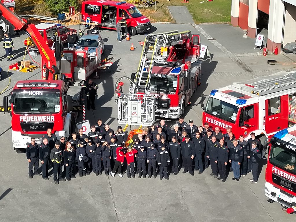 Feuerwehrmitglieder stehen für ein Gruppenfoto vor mehreren roten Einsatzfahrzeugen der Freiwilligen Feuerwehr Horn.