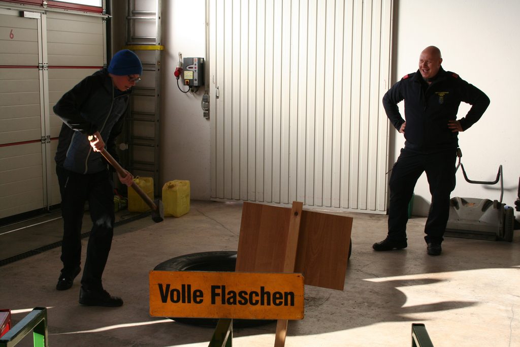 Ein Besucher probiert unter Anleitung eines Feuerwehrmitglieds eine Geschicklichkeitsstation mit Holzhammer und Reifen aus.