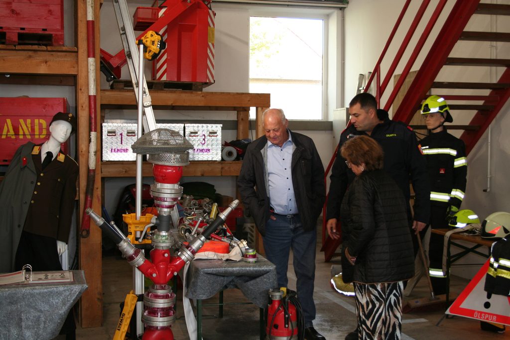Besucher betrachten Feuerwehrgegenstände, Armaturen und moderne Schutzausrüstung im Feuerwehrhaus.