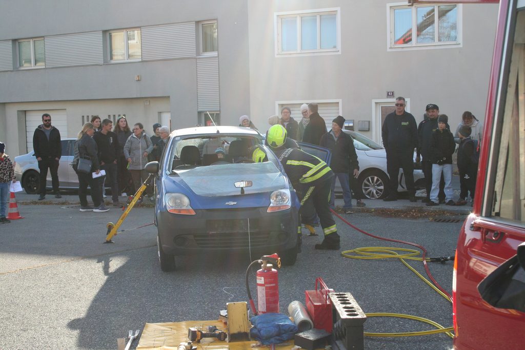 Feuerwehrmitglieder zeigen an einem Pkw die technische Rettung, während Besucherinnen und Besucher die Vorführung beobachten.